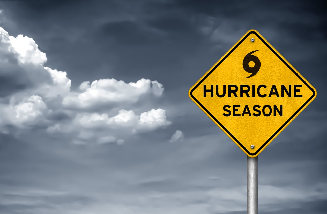A cloudy, gray, stormy sky, with a yellow diamond caution sign that reads “hurricane season” followed by a hurricane weather symbol.